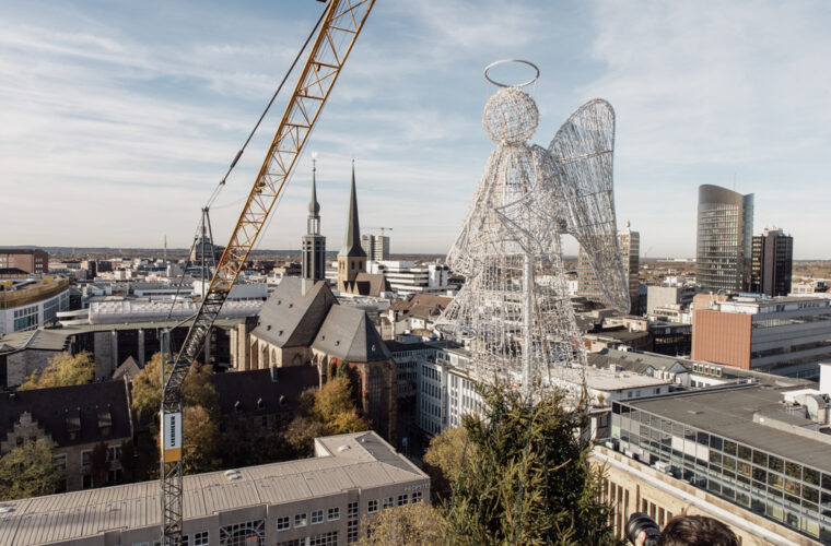 Ein vier meter großer Leuchtengel steckt auf der Spitze der großen Baumkonstruktion vor der Stadtkulisse.