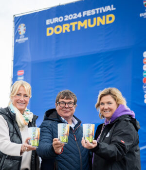 Claudia Branz (Dicke & Partner), Schausteller Patrick Arens und Simone Karcz (Stadt Dortmund) präsentieren die Fußball-Tasse.